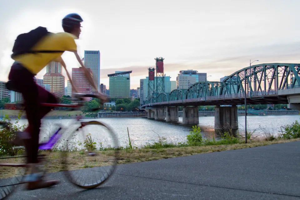 Cyclist on bike path in Portland, Oregon with bridge over river and city skyline in background.